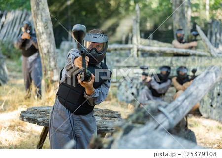 Woman in protective clothes and helmet aiming with paintball marker 125379108