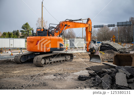 broken asphalt and orange excavator at road construction site, roadwork concept 125380131