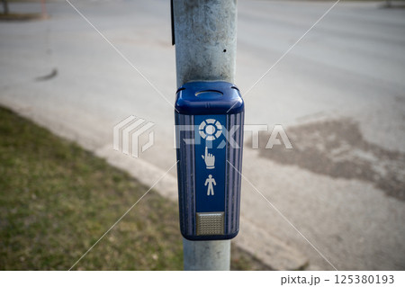 Pedestrian crossing button mounted on a metal pole beside a road 125380193