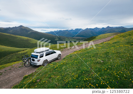 Offroad car carrying bikes on flowering grassland mountain under blue sky 125380722