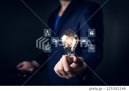 A person in a suit holds a glowing lightbulb featuring AI-related icons such as gears, graphs, and media, symbolizing innovation, creativity, and the ability to generate intelligent solutions. 125381146