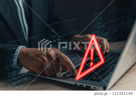 A professional uses a laptop displaying a glowing red warning triangle with an exclamation mark, symbolizing caution and cybersecurity threats in a digital environment filled with code. A professional uses a laptop displaying a glowing red warning triangle with an exclamation mark, symbolizing caution and cybersecurity threats in a digital environment filled with code. 125381149