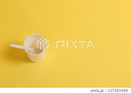 Disposable paper cup with a teaspoon on a yellow background. Disposable paper cup with a teaspoon on a yellow background. 125381409