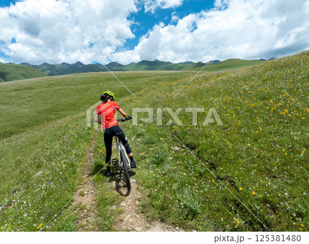 Aerial view of riding mountain bike on flowering grassland mountain Aerial view of riding mountain bike on flowering grassland mountain 125381480