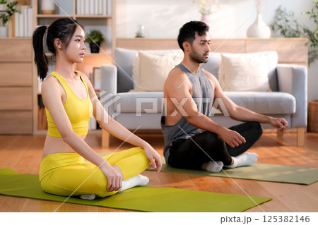 Young asian couple practicing yoga and meditation together in the living room at home. 125382146