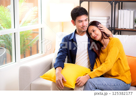 Portrait young asian couple hold hands sitting on sofa looking affectionate and embrace. 125382177