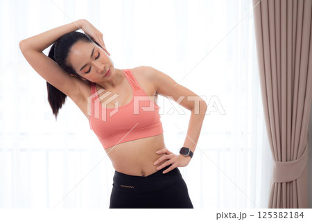Beautiful young asian woman standing workout with warmup and stretch muscle neck at home. 125382184