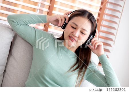 Happy young asian woman wearing headphones listening music while sitting on sofa with fun. Happy young asian woman wearing headphones listening music while sitting on sofa with fun. 125382201