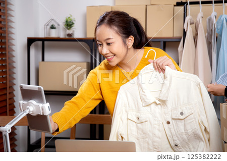 Two young asian woman live online clothing store while showing clothing with tablet and laptop. 125382222