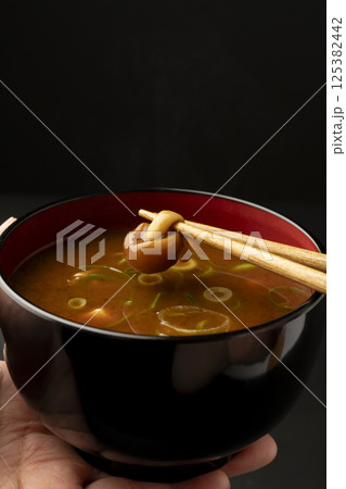赤味噌を使ったなめこと豆腐の味噌汁のなめこを箸で持ち上げる 125382442