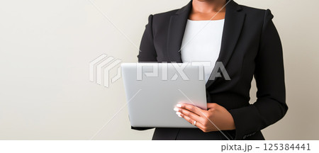 African female adult professional holding tablet in black suit against neutral background 125384441