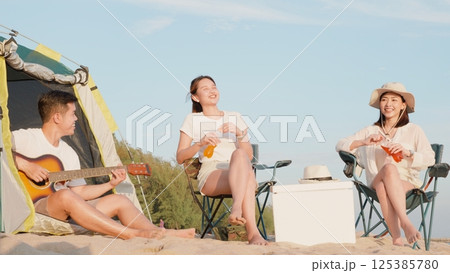 Happy friends with drinks in camp and laughing together in holidays on sand beach near camping tent vacation time at sunset, Young Asian group woman and man in summer travel outdoor 125385780