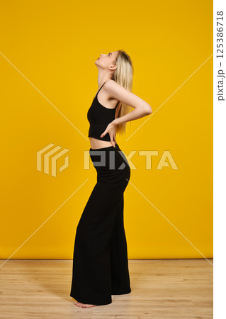 Model posing in black outfit against vibrant yellow background in studio setting Model posing in black outfit against vibrant yellow background in studio setting 125386718