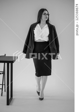 Professional woman walking in modern office space, wearing black suit and white top, serious expression 125388674