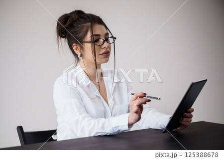 Young woman in white shirt reviewing documents on tablet at desk 125388678