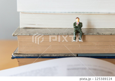 机の上に開いた英語の書籍とスーツの男性フィギア 研究 学習 学び直しのイメージ 机の上に開いた英語の書籍とスーツの男性フィギア 研究 学習 学び直しのイメージ 125389114