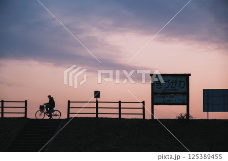 [流れ橋]美しい夕日をバックに自転車に乗る人 125389455