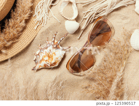 Sunglasses, seashells, pampas grass and rattan hat on sandy beach, top view Sunglasses, seashells, pampas grass and rattan hat on sandy beach, top view 125390517