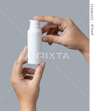 Female hands holding white cosmetic pump bottle against grey close up, mockup, copy space 125390553