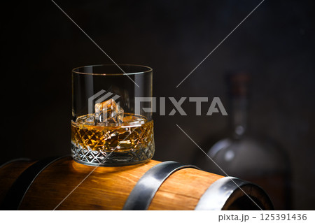 A glass of whiskey with ice cubes on old oak barrel A glass of whiskey with ice cubes on old oak barrel 125391436