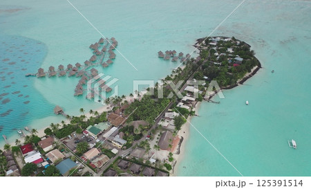 Aerial view of luxurious overwater bungalows in tropical turquoise lagoon surrounding exotic island with lush vegetation and buildings, showcasing the beauty of Bora Bora Aerial view of luxurious overwater bungalows in tropical turquoise lagoon surrounding exotic island with lush vegetation and buildings, showcasing the beauty of Bora Bora 125391514