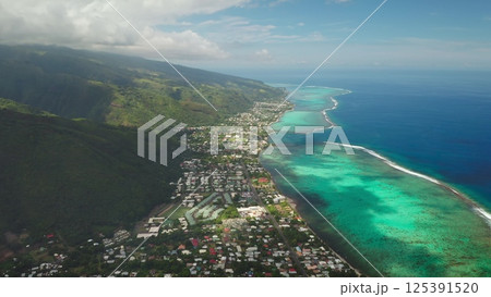 Capturing stunning aerial views of a tropical coastline where lush green mountains meet vibrant turquoise waters, revealing a picturesque town nestled in nature's beauty 125391520