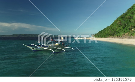 Aerial drone view of a traditional banca boat sailing on turquoise water near a white sand beach with lush vegetation on Apo Island, Philippines, showcasing the beauty of a tropical paradise Aerial drone view of a traditional banca boat sailing on turquoise water near a white sand beach with lush vegetation on Apo Island, Philippines, showcasing the beauty of a tropical paradise 125391579