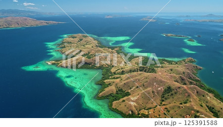 Breathtaking aerial view of Komodo national park in Indonesia, featuring vibrant turquoise waters caressing lush, hilly islands beneath a clear blue sky 125391588