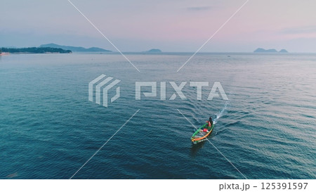 Aerial view of a small fishing boat navigating the calm waters of a tropical sea at sunset, with islands and coastline visible in the distance, creating a serene and picturesque scene 125391597