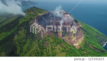 White smoke billowing from the crater of Mount Iliwerung volcano on Flores Island, Indonesia, surrounded by lush green vegetation and the blue ocean White smoke billowing from the crater of Mount Iliwerung volcano on Flores Island, Indonesia, surrounded by lush green vegetation and the blue ocean 125391615