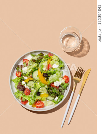 Vegetable salad with lettuce, vegetables, olives and feta cheese on beige background Vegetable salad with lettuce, vegetables, olives and feta cheese on beige background 125394843