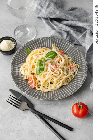 Creamy spaghetti with cherry tomatoes, parmesan cheese and basil on a plate on a light background 125394846