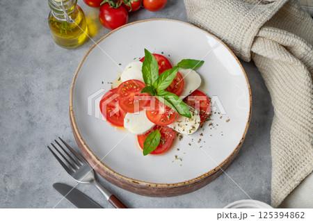 Caprese salad with slice tomatoes, mozzarella and basil on a plate on a light background Caprese salad with slice tomatoes, mozzarella and basil on a plate on a light background 125394862