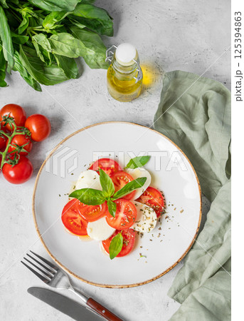 Fresh Caprese salad with tomatoes, mozzarella and basil on a plate on light background. 125394863