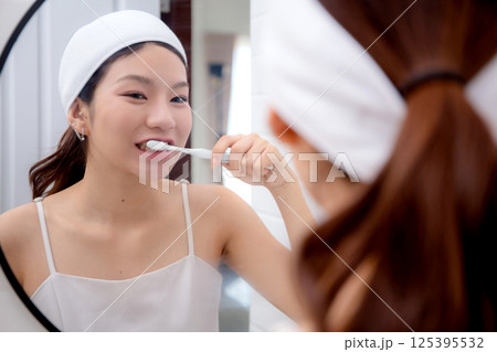 Happy young asian woman brush teeth looking mirror at home, woman clean teeth in bathroom. 125395532
