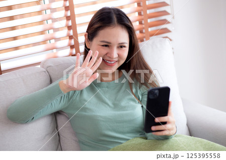 Young asian woman sitting on sofa looking smartphone for video call in living room. Young asian woman sitting on sofa looking smartphone for video call in living room. 125395558