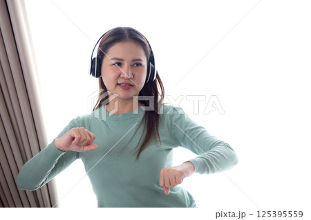 Happy young asian woman wearing headphones listening music while standing dancing with fun. Happy young asian woman wearing headphones listening music while standing dancing with fun. 125395559