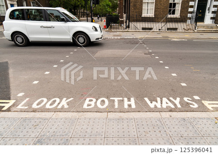 A street in London with the phrase LOOK BOTH WAYS painted on the road, indicating the pedestrian crossing. Traffic lights are visible, showing a red signal, and classic London style buildings 125396041