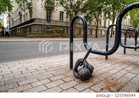 A kettlebell is secured to a bike rack on a quiet city sidewalk, drawing attention in the everyday urban scene. A kettlebell is secured to a bike rack on a quiet city sidewalk, drawing attention in the everyday urban scene. 125396044