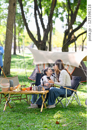 Happy mother feeds her smiling daughter during a family camping breakfast outdoors 125396118