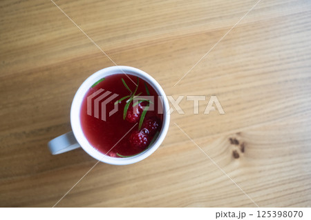 Raspberry tea in a white mug on a wooden table. 125398070