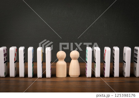 Wooden Figurines Between Falling Dominoes Symbolizing Cause and Effect 125398176