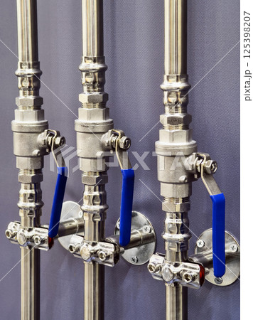 Detailed close-up of industrial piping system with blue handles showcasing valve mechanisms and stainless steel fittings Detailed close-up of industrial piping system with blue handles showcasing valve mechanisms and stainless steel fittings 125398207