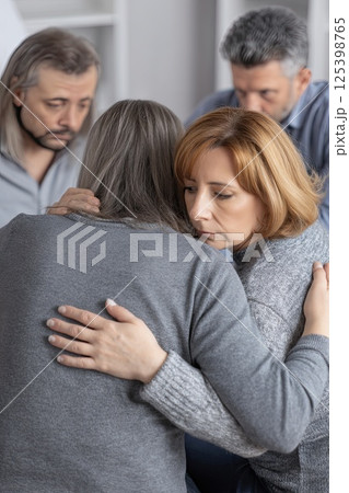 Group therapy and support - middle aged men and women hug, supporting each other during psychological practice. The healing power of hugs creates a safe space for members. Vertical photo 125398765
