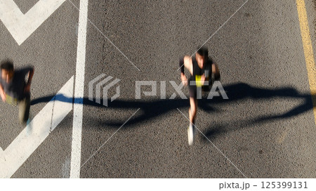 Aerial view of marathon runners on urban road with chevron markings, blurred motion capturing speed and movement of competitors 125399131