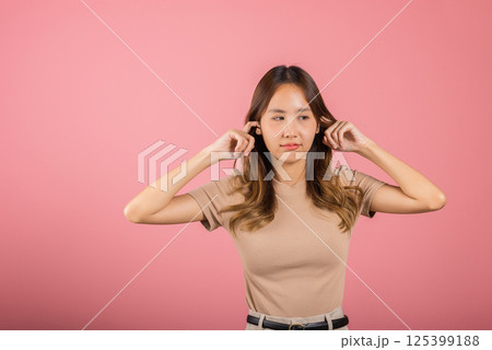 Woman bad mood pain her closed ears with finger and close eyes, Asian beautiful young female covers ears for loud noise, studio shot isolated on pink background with copy space, bad pressure 125399188