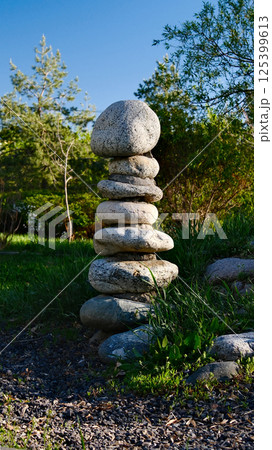 Zen garden meditation space with carefully balanced stone cairn, natural rock formations, lush green grass 125399613