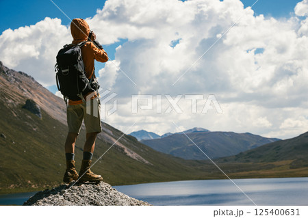 Woman photographer taking picture on high altitude mountain top,with a lake in the distance 125400631