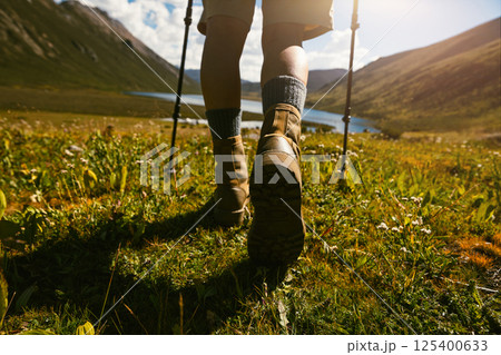 Hiker legs wearing leather boots hiking on high altitude mountain top,with a lake in the distance 125400633