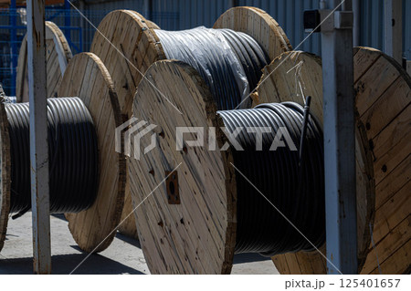 Wooden spools with black cable wires stacked in a row at a manufacturing yard. Wooden spools with black cable wires stacked in a row at a manufacturing yard. 125401657